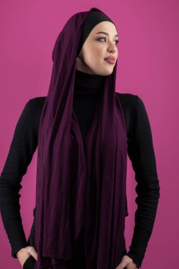 Başörtülü çarpıcı bir Müslüman kadın zarif bir şekilde stüdyoda pembe bir arka plana karşı poz veriyor, zarafet ve güven yayıyor.. 