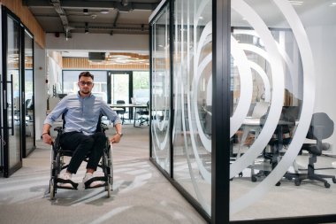 Büyük, modern bir şirkette, tekerlekli sandalyedeki kararlı bir işadamı bir koridorda dolaşır, kurumsal dünyaya güç ve kapsayıcılık kazandırır.