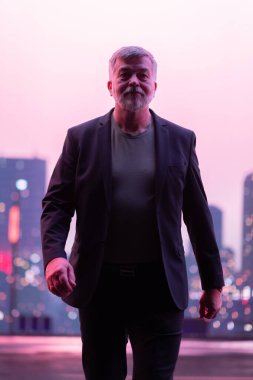 Şık takım elbiseli kendinden emin bir üst sınıf öğrencisi alacakaranlıkta parlayan şehir siluetine karşı kameraya doğru yürüyor.. 