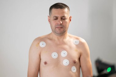 Orta yaşlı bir adam, klinik bir ortamda kalp izleme için EKG elektrotlarına bağlı bir koşu bandında tıbbi stres testinden geçiyor.. 