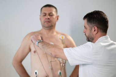 Orta yaşlı bir adam, klinik bir ortamda kalp izleme için EKG elektrotlarına bağlı bir koşu bandında tıbbi stres testinden geçiyor.. 