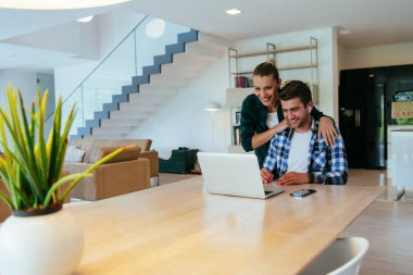 Genç evli bir çift, modern evlerinin oturma odasında otururken bir dizüstü bilgisayarla ebeveynleri, aileleri ve arkadaşlarıyla konuşuyor.