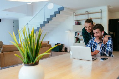 Genç evli bir çift, modern evlerinin oturma odasında otururken bir dizüstü bilgisayarla ebeveynleri, aileleri ve arkadaşlarıyla konuşuyor.