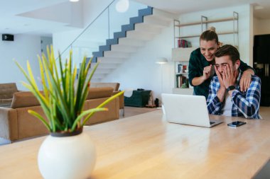 Genç evli bir çift, modern evlerinin oturma odasında otururken bir dizüstü bilgisayarla ebeveynleri, aileleri ve arkadaşlarıyla konuşuyor.