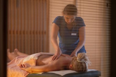Spa 'da Sırt Masajı. Mavi üniformalı profesyonel bir masaj terapisti masaj masasında yatan bir müşteriye rahatlatıcı bir sırt masajı sağlar.