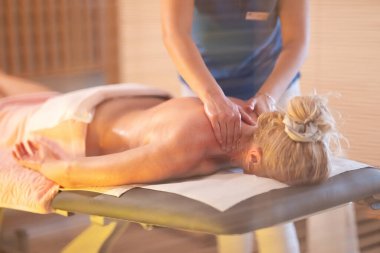 Spa 'da Sırt Masajı. Mavi üniformalı profesyonel bir masaj terapisti masaj masasında yatan bir müşteriye rahatlatıcı bir sırt masajı sağlar.