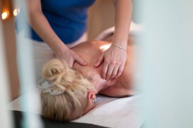 Spa 'da Sırt Masajı. Mavi üniformalı profesyonel bir masaj terapisti masaj masasında yatan bir müşteriye rahatlatıcı bir sırt masajı sağlar.