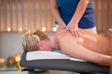 Spa 'da Sırt Masajı. Mavi üniformalı profesyonel bir masaj terapisti masaj masasında yatan bir müşteriye rahatlatıcı bir sırt masajı sağlar.