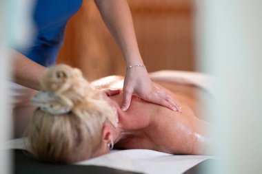 Spa 'da Sırt Masajı. Mavi üniformalı profesyonel bir masaj terapisti masaj masasında yatan bir müşteriye rahatlatıcı bir sırt masajı sağlar.