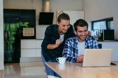 Genç evli bir çift, modern evlerinin oturma odasında otururken bir dizüstü bilgisayarla ebeveynleri, aileleri ve arkadaşlarıyla konuşuyor.