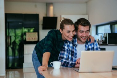 Genç evli bir çift, modern evlerinin oturma odasında otururken bir dizüstü bilgisayarla ebeveynleri, aileleri ve arkadaşlarıyla konuşuyor.