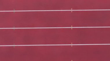 Boş koşu pistinin yukarıdan aşağıya görüntüsü, el değmemiş şeritleri, temiz sınırları ve geniş açık alanı gösteriyor, pistin dinginliğini ve yalnızlığını vurguluyor, spor ve uygunluk için ideal.