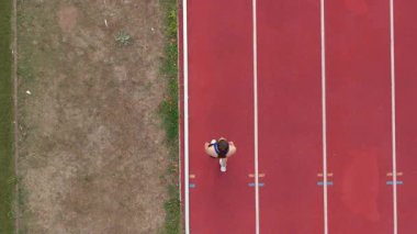 Büyük bir stadyum atletizm pistinde koşan profesyonel bir bayan sporcunun havadan drone görüntüsü. Dinamik yavaş çekim sinematik görüntüler onun gücünü, hızını ve kararlılığını yakalar.