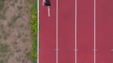 Büyük bir stadyum atletizm pistinde koşan profesyonel bir bayan sporcunun havadan drone görüntüsü. Dinamik yavaş çekim sinematik görüntüler onun gücünü, hızını ve kararlılığını yakalar.
