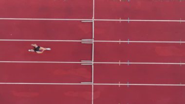 Büyük bir stadyum atletizm pistinde koşan profesyonel bir bayan sporcunun havadan drone görüntüsü. Dinamik yavaş çekim sinematik görüntüler onun gücünü, hızını ve kararlılığını yakalar.