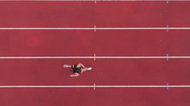 Büyük bir stadyum atletizm pistinde koşan profesyonel bir bayan sporcunun havadan drone görüntüsü. Dinamik yavaş çekim sinematik görüntüler onun gücünü, hızını ve kararlılığını yakalar.