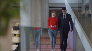 Modern bir girişim şirketinin dinamik ortamında, yönetici genç iş arkadaşı ile yürürken bir tartışma içine girer, işbirliği ve yenilik ruhunu yansıtır.