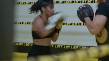 Kickboks yapan kadın boksör yumruklarını çalıştırırken kız hızlı saldırırken spor salonunda günlük antrenman yapıyor. Yüksek kalite 8K görüntü
