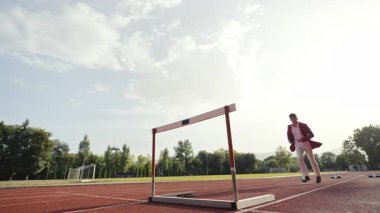 İş adamı atletizm pistinde koşarken engelden atlıyor. Yüksek kalite 4 bin yavaş çekim görüntüsü