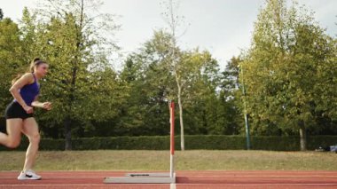 Dişi sporcu bir engele doğru koşuyor, engelli koşuyor, yüksek hızda bariyerin üzerinden atlıyor bir yarışta koşarken. Hız Rampası Efektli Süper Yavaş Sinema Görüntüsü.