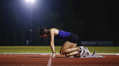 Atletizm atletizm sprint yarışı koşucusu koyu bir arka planda, stadyumun pistinde spor ayakkabılarla koşu koşusuna çıkıyor. Yavaş çekim
