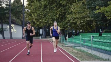 Stadyumun kırmızı raylarında egzersiz yaparken koşan iki zinde erkek ve kadın. Yüksek kalite 4 bin yavaş çekim görüntüsü