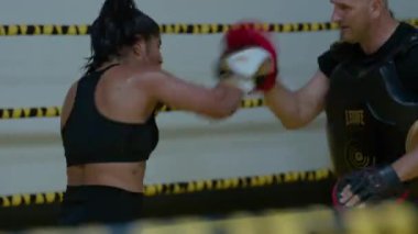 Kickboks yapan kadın boksör yumruklarını çalıştırırken kız hızlı saldırırken spor salonunda günlük antrenman yapıyor. Yüksek kalite 8K görüntü
