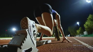 Atletizm atletizm sprint yarışı koşucusu koyu bir arka planda, stadyumun pistinde spor ayakkabılarla koşu koşusuna çıkıyor. Yavaş çekim