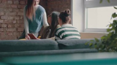 Kadın iş adamları pencere kenarında iş birliği yapıyor, fikirleri tartışıyor ve tablet üzerinde beyin fırtınası yapıyorlar. Modern bir ofiste işbirliği, yaratıcılık ve takım çalışması kavramı