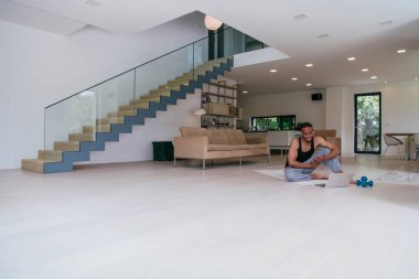 Evde antrenman. Spor düşkünü Afrikalı Amerikalı bir adam dizüstü bilgisayar başında eğitim alırken, oturma odasında egzersiz yaparken, boş bir alanda..