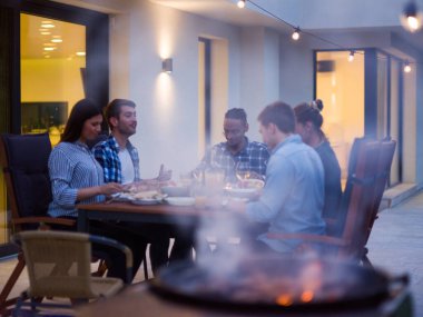Bir grup genç insan akşamları modern bir evin terasında yemek yiyorlar. Dostlar ve aile için eğlence. Tatil kutlamaları, barbekülü düğünler..