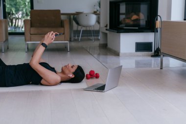 Modern evde dinlenirken ve yerde yatarken akıllı telefon kullanan bir sporcu kadın.. 