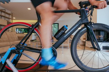 Modern bir oturma odasında triatlon bisikleti süren bir triatloncu. Pandemik koşullarda eğitim