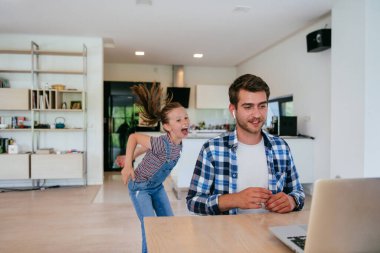 Evden çalışıyorum. Kızı, modern oturma odasında otururken bilgisayarında iş görüşmesi yaparken babasının sözünü kesiyor.