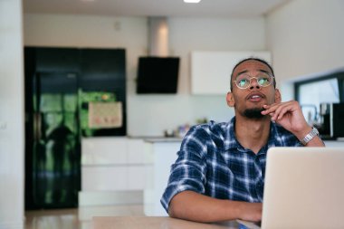 Modern bir oturma odasındaki masada oturan gözlüklü Afrikalı Amerikalı etkileyiciler iş görüşmesi, arkadaşlarla sohbet ve eğlence için dizüstü bilgisayar kullanıyorlar.