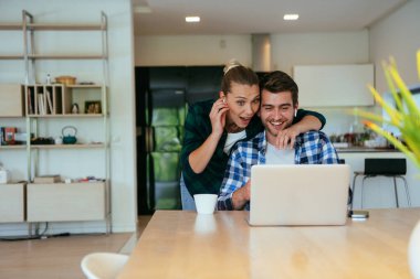 Genç evli bir çift, modern evlerinin oturma odasında otururken bir dizüstü bilgisayarla ebeveynleri, aileleri ve arkadaşlarıyla konuşuyor.