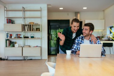 Genç evli bir çift, modern evlerinin oturma odasında otururken bir dizüstü bilgisayarla ebeveynleri, aileleri ve arkadaşlarıyla konuşuyor.