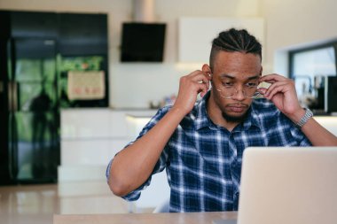 Modern bir oturma odasındaki masada oturan gözlüklü Afrikalı Amerikalı etkileyiciler iş görüşmesi, arkadaşlarla sohbet ve eğlence için dizüstü bilgisayar kullanıyorlar.