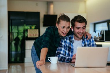 Genç evli bir çift, modern evlerinin oturma odasında otururken bir dizüstü bilgisayarla ebeveynleri, aileleri ve arkadaşlarıyla konuşuyor.