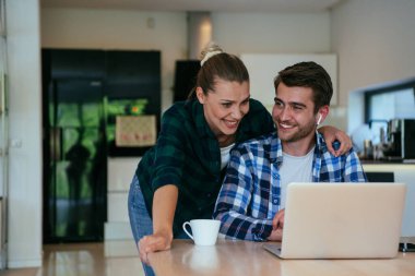 Genç evli bir çift, modern evlerinin oturma odasında otururken bir dizüstü bilgisayarla ebeveynleri, aileleri ve arkadaşlarıyla konuşuyor.