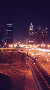 Parlayan gece trafiğinin, akıllı Dubai şehrindeki fütüristik gökdelenlerle çevrili otoyol kavşaklarından dokumasının en üst görüntüsü. Canlı şehir ışıkları, modern ufuk çizgisi ve şehir mimarisi.