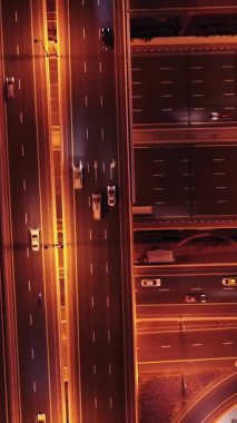 Parlayan gece trafiğinin, akıllı Dubai şehrindeki fütüristik gökdelenlerle çevrili otoyol kavşaklarından dokumasının en üst görüntüsü. Canlı şehir ışıkları, modern ufuk çizgisi ve şehir mimarisi.