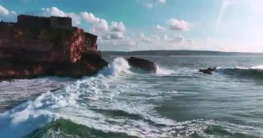 Güneş batarken kayalık bir kıyıya çarpan derin mavi okyanus dalgalarının dramatik hava manzarası bu sakin tropikal deniz manzarasını güzelleştirir. Seyahat, tatil ve doğa temaları için mükemmeldir..