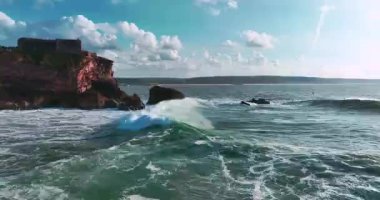 Güneş batarken kayalık bir kıyıya çarpan derin mavi okyanus dalgalarının dramatik hava manzarası bu sakin tropikal deniz manzarasını güzelleştirir. Seyahat, tatil ve doğa temaları için mükemmeldir..