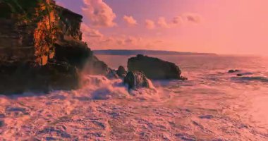 Güneş batarken kayalık bir kıyıya çarpan derin mavi okyanus dalgalarının dramatik hava manzarası bu sakin tropikal deniz manzarasını güzelleştirir. Seyahat, tatil ve doğa temaları için mükemmeldir..