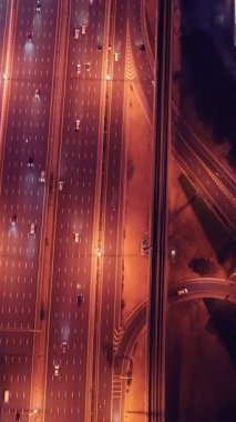 Parlayan gece trafiğinin, akıllı Dubai şehrindeki fütüristik gökdelenlerle çevrili otoyol kavşaklarından dokumasının en üst görüntüsü. Canlı şehir ışıkları, modern ufuk çizgisi ve şehir mimarisi.