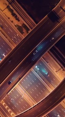 Parlayan gece trafiğinin, akıllı Dubai şehrindeki fütüristik gökdelenlerle çevrili otoyol kavşaklarından dokumasının en üst görüntüsü. Canlı şehir ışıkları, modern ufuk çizgisi ve şehir mimarisi.