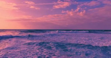 Güneş batarken kayalık bir kıyıya çarpan derin mavi okyanus dalgalarının dramatik hava manzarası bu sakin tropikal deniz manzarasını güzelleştirir. Seyahat, tatil ve doğa temaları için mükemmeldir..