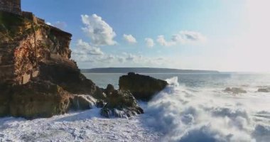 Güneş batarken kayalık bir kıyıya çarpan derin mavi okyanus dalgalarının dramatik hava manzarası bu sakin tropikal deniz manzarasını güzelleştirir. Seyahat, tatil ve doğa temaları için mükemmeldir..
