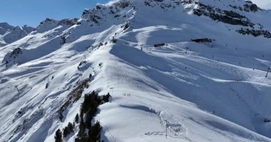 Karla kaplı dağların, güneşli gökyüzünün ve kayak, snowboard, yürüyüş ve açık hava maceraları için mükemmel manzaralı yamaçların nefes kesici hava manzarası.